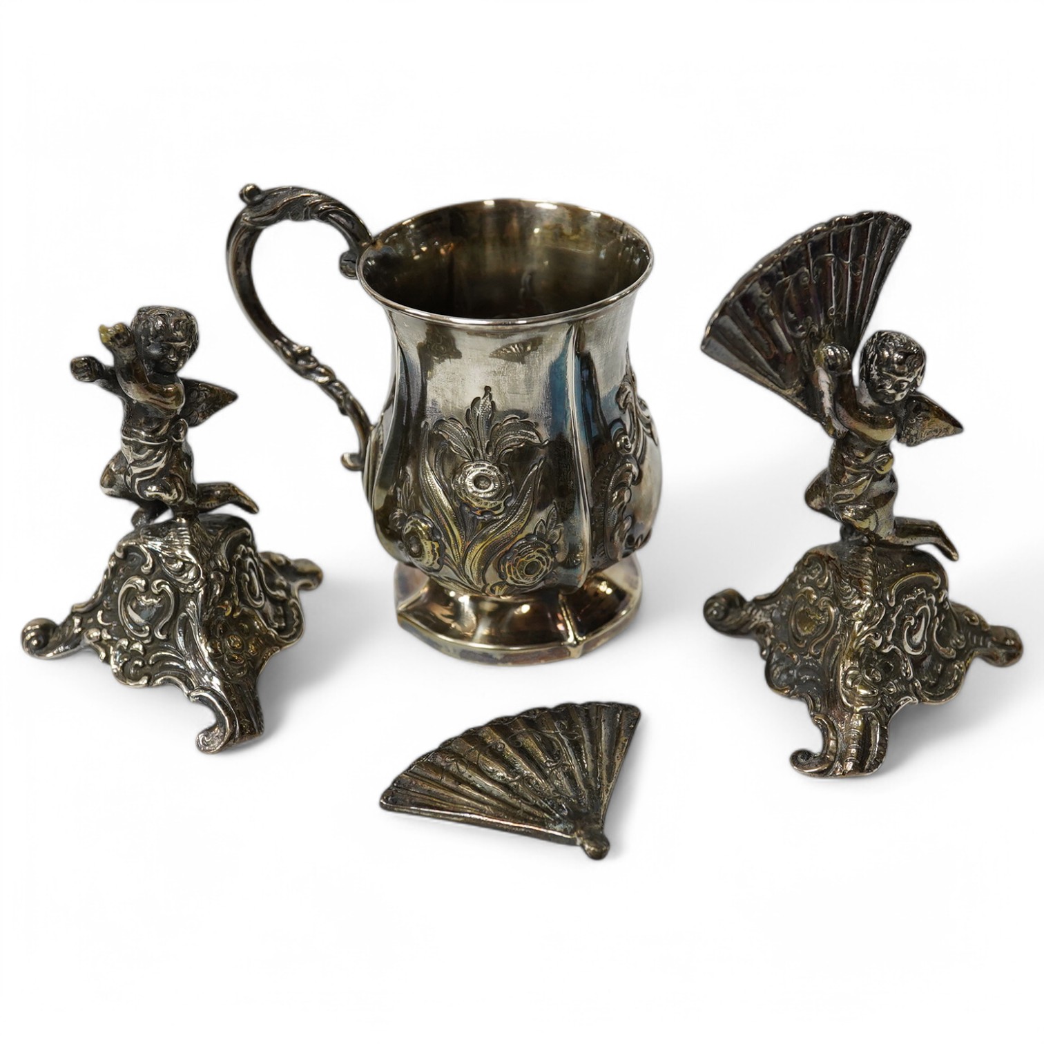 A small Victorian silver christening mug with embossed decoration and scroll handle, Hilliard & Thomason, Birmingham, 1860, 82mm and a pair of cast silver cherub figures holding fan, (Chester import marks) on triangular